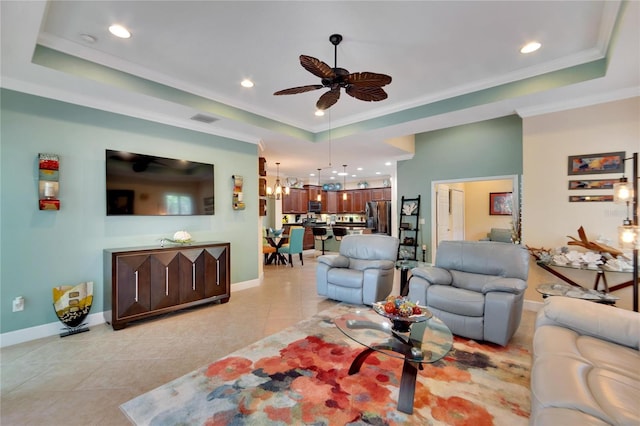 tiled living room featuring ceiling fan with notable chandelier, a tray ceiling, and ornamental molding