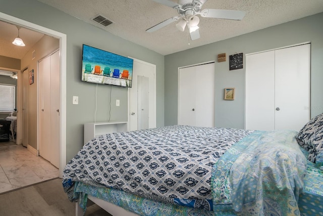 bedroom with two closets, ceiling fan, and a textured ceiling