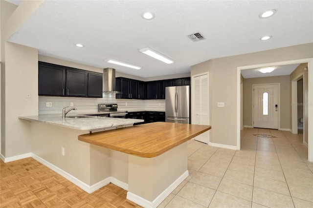 kitchen featuring wall chimney range hood, sink, appliances with stainless steel finishes, decorative backsplash, and kitchen peninsula