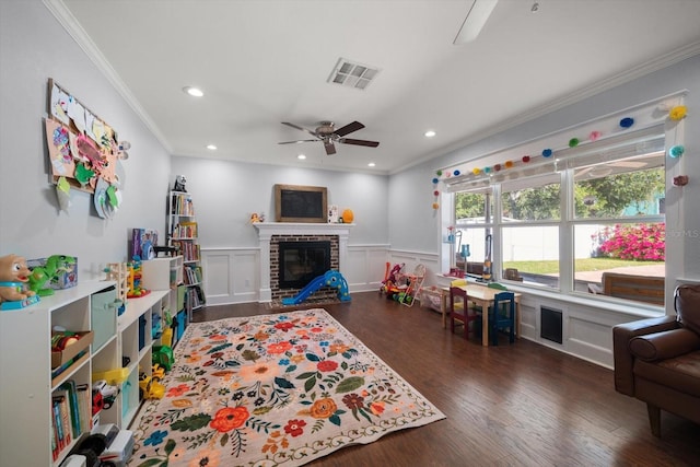 rec room with ceiling fan, a fireplace, dark hardwood / wood-style flooring, and crown molding