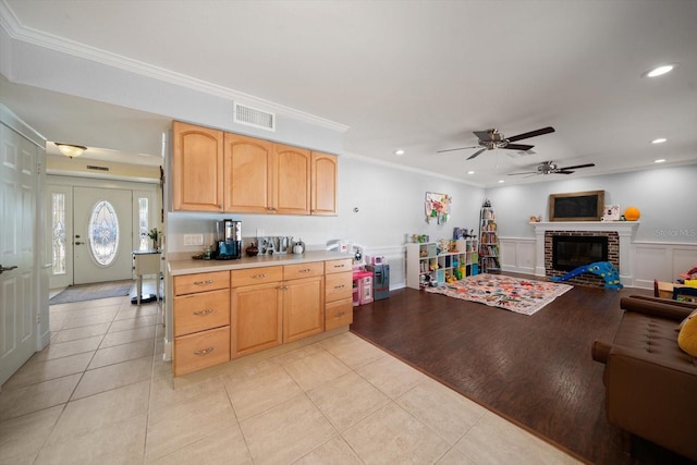 kitchen with light brown cabinets, crown molding, a brick fireplace, ceiling fan, and light tile patterned flooring