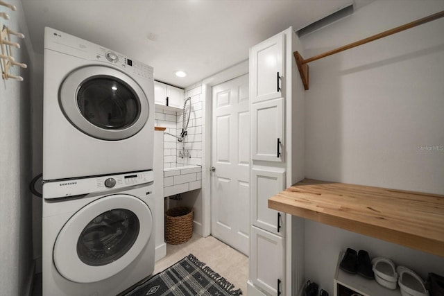 laundry room with light tile patterned flooring, cabinets, and stacked washer and clothes dryer