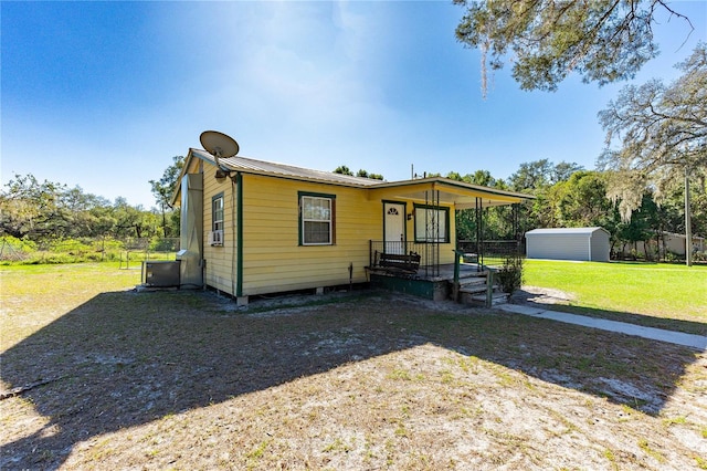 view of front of house featuring central AC, covered porch, a front yard, and a storage shed