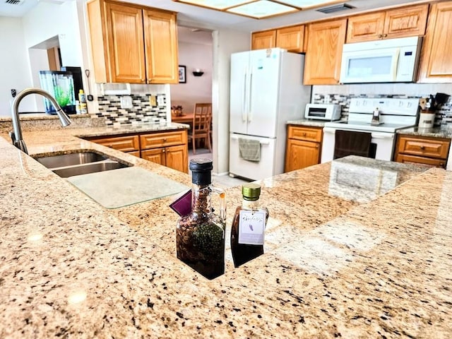 kitchen featuring white appliances, light stone countertops, sink, and decorative backsplash