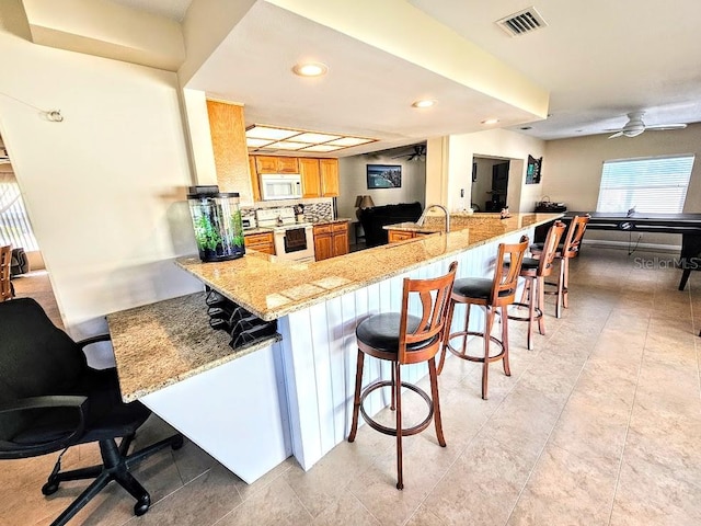 kitchen featuring white appliances, a kitchen breakfast bar, ceiling fan, decorative backsplash, and kitchen peninsula