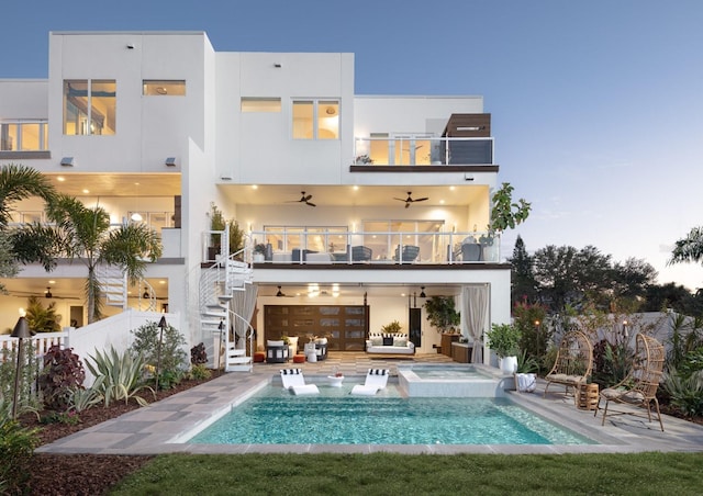 back house at dusk with an outdoor hangout area, a pool with hot tub, ceiling fan, a balcony, and a patio area