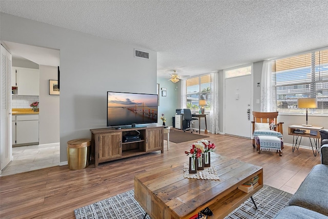 living room with ceiling fan, a textured ceiling, and light wood-type flooring