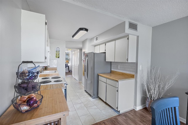 kitchen featuring tasteful backsplash, a textured ceiling, light hardwood / wood-style floors, white cabinetry, and stainless steel refrigerator