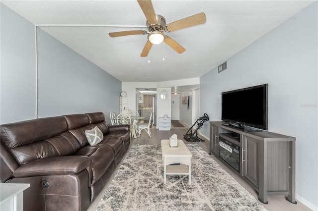 living room with ceiling fan, a textured ceiling, and light hardwood / wood-style flooring