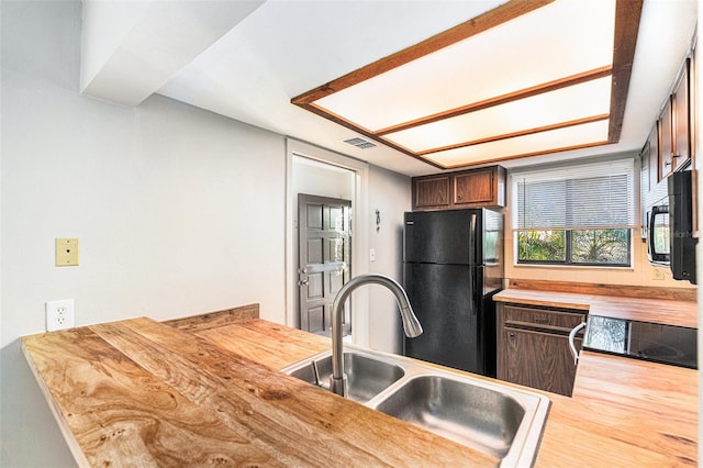 kitchen featuring black appliances, butcher block counters, dark brown cabinetry, and sink