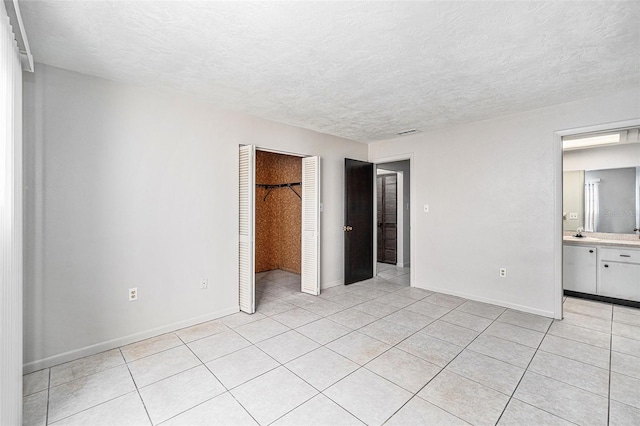 unfurnished bedroom featuring sink, ensuite bath, light tile patterned floors, a textured ceiling, and a closet