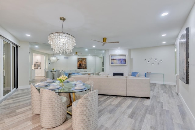 dining area with ceiling fan with notable chandelier, light hardwood / wood-style flooring, and a fireplace