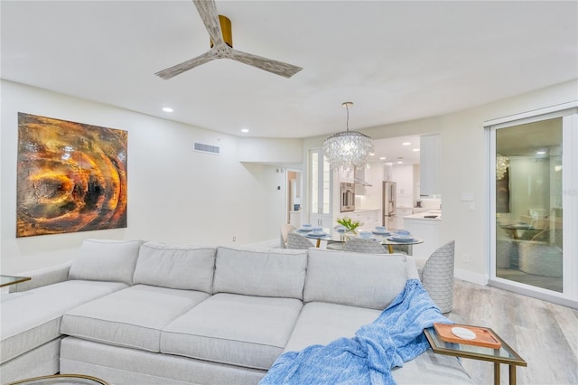 living room with ceiling fan with notable chandelier and light hardwood / wood-style flooring