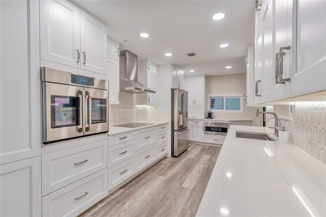 kitchen with light hardwood / wood-style floors, sink, white cabinetry, appliances with stainless steel finishes, and wall chimney exhaust hood