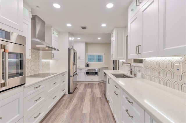 kitchen featuring stainless steel appliances, wall chimney exhaust hood, white cabinetry, and sink