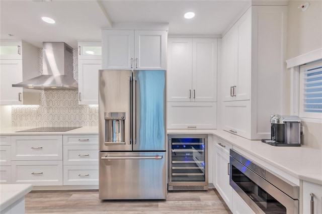 kitchen with appliances with stainless steel finishes, backsplash, wine cooler, wall chimney range hood, and white cabinets