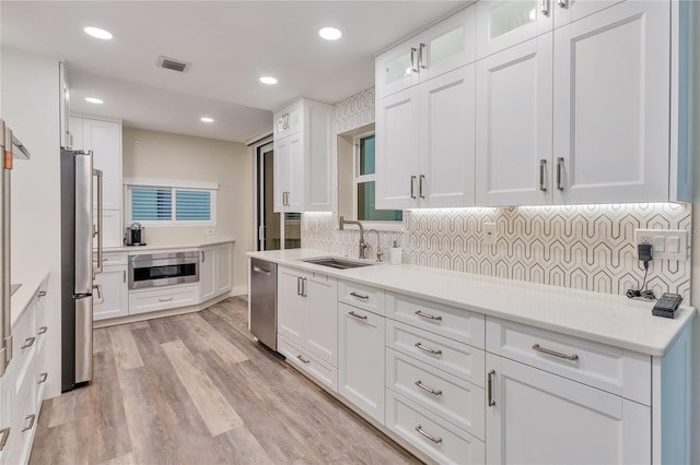 kitchen with appliances with stainless steel finishes, white cabinetry, decorative backsplash, sink, and light hardwood / wood-style flooring