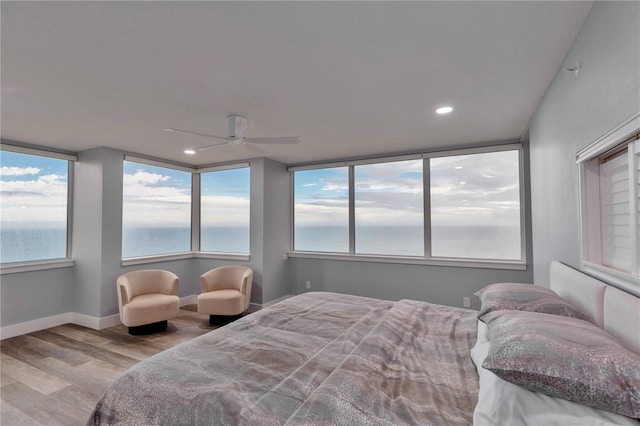 bedroom featuring ceiling fan, light hardwood / wood-style flooring, and a water view