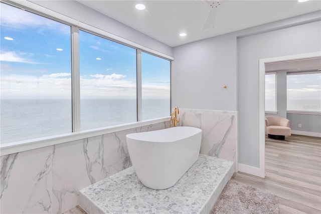 bathroom featuring a water view, a tub, a wealth of natural light, and hardwood / wood-style floors