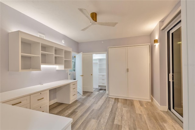 unfurnished office with ceiling fan, built in desk, and light wood-type flooring