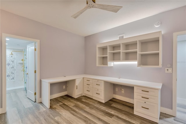 unfurnished office with built in desk, ceiling fan, and light wood-type flooring