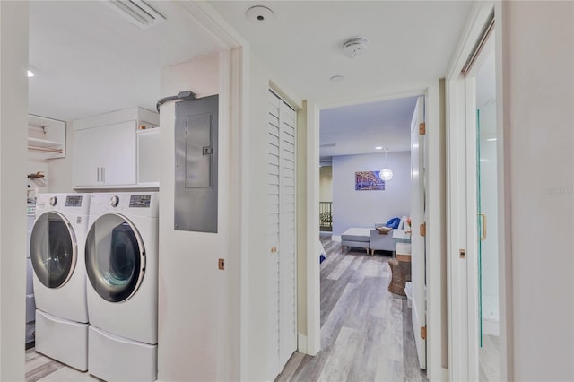 clothes washing area with washing machine and dryer, cabinets, electric panel, and light wood-type flooring