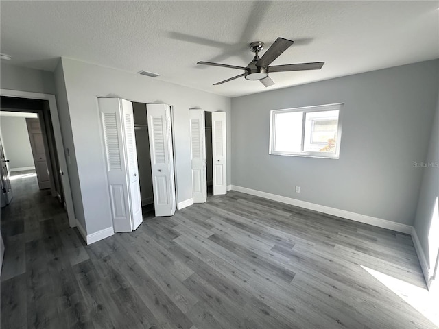 unfurnished bedroom featuring multiple closets, ceiling fan, hardwood / wood-style floors, and a textured ceiling