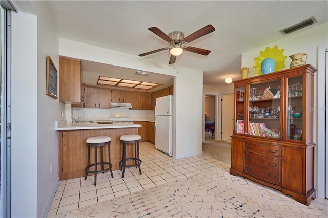 kitchen featuring ceiling fan, ventilation hood, kitchen peninsula, a textured ceiling, and white appliances