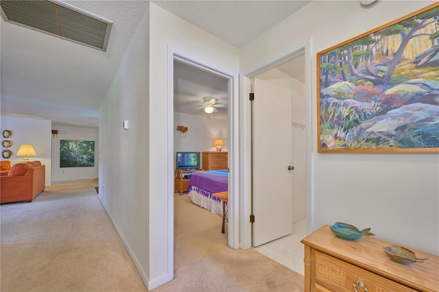 corridor with a textured ceiling and light colored carpet