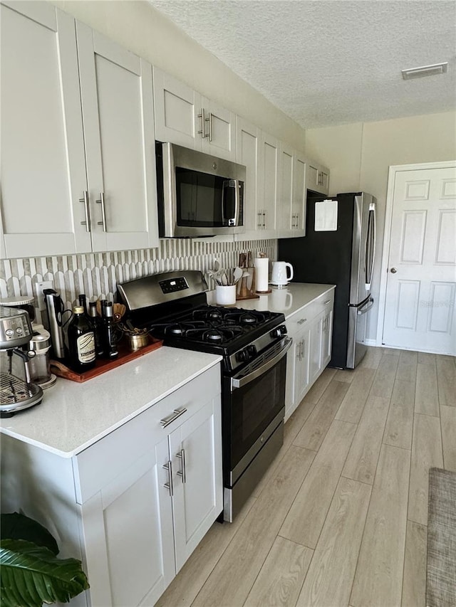 kitchen featuring light hardwood / wood-style flooring, white cabinets, a textured ceiling, and appliances with stainless steel finishes