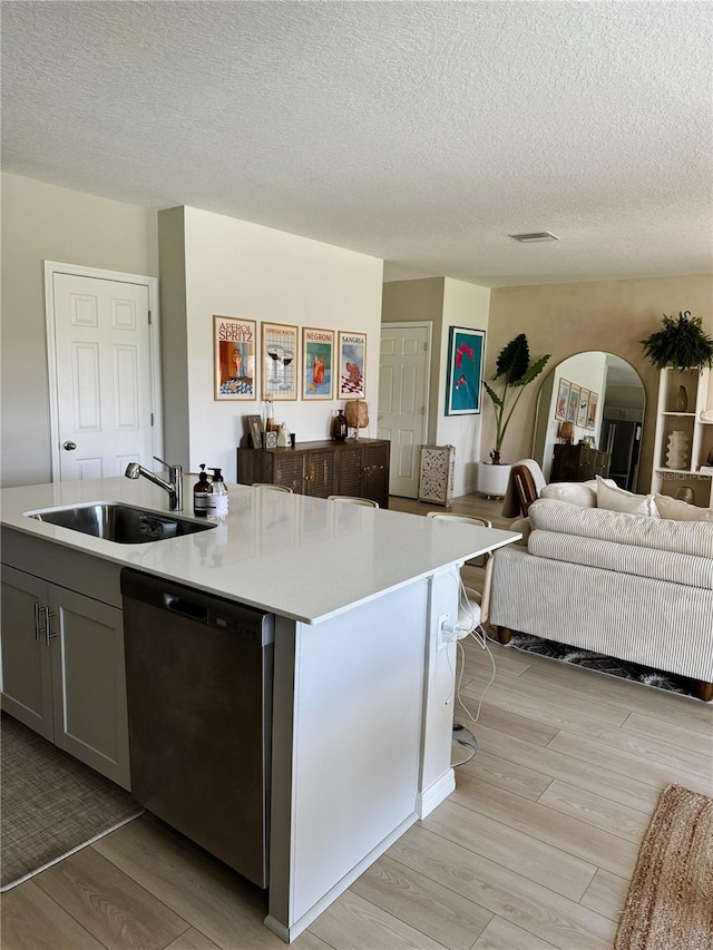 kitchen with light wood-type flooring, a textured ceiling, sink, a center island with sink, and dishwasher