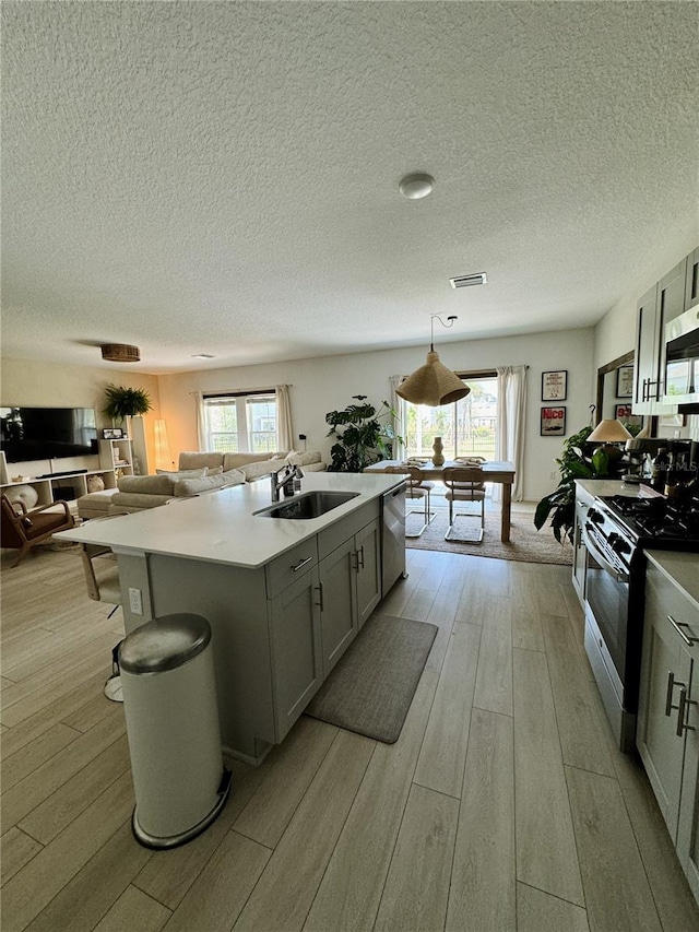 kitchen featuring hanging light fixtures, appliances with stainless steel finishes, a wealth of natural light, and a kitchen island with sink