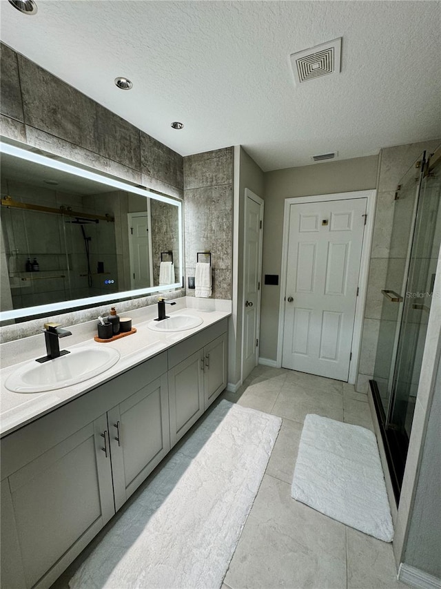 bathroom with tile patterned flooring, vanity, a shower with shower door, and a textured ceiling