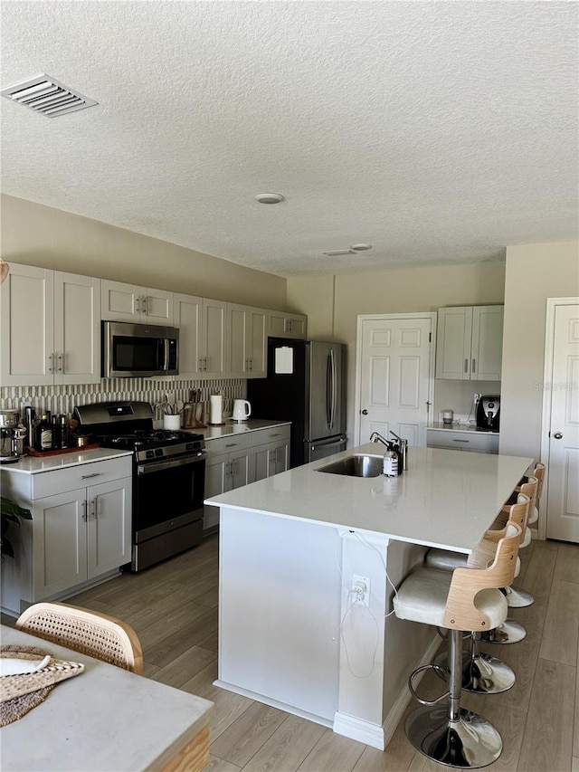 kitchen featuring sink, stainless steel appliances, hardwood / wood-style floors, decorative backsplash, and a center island with sink