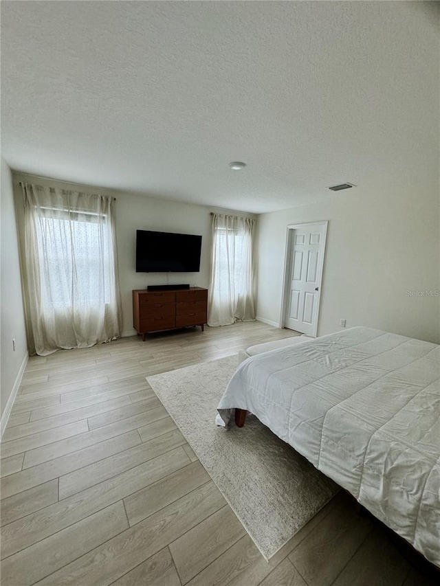 unfurnished bedroom with a textured ceiling, light wood-type flooring, and multiple windows