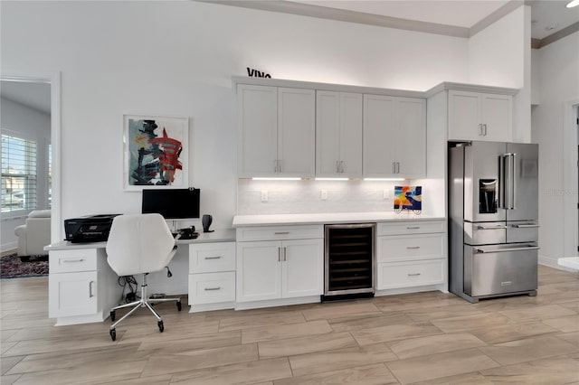 kitchen with wine cooler, tasteful backsplash, built in desk, high quality fridge, and white cabinets