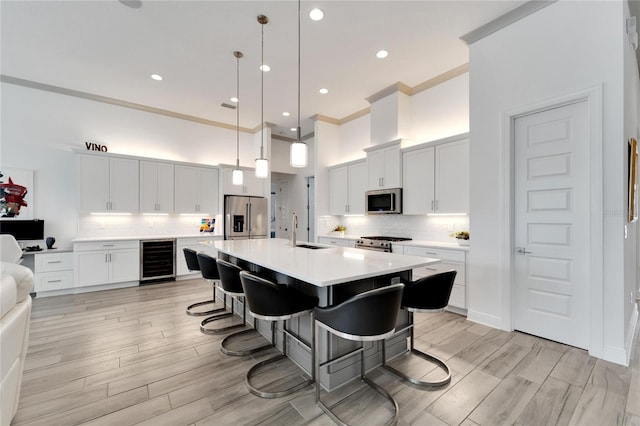 kitchen featuring premium appliances, an island with sink, wine cooler, pendant lighting, and white cabinets