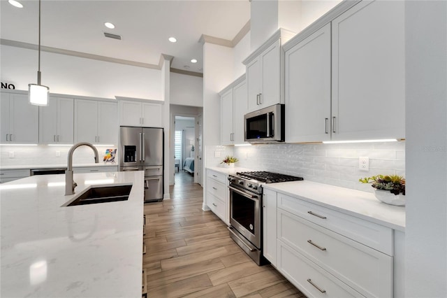 kitchen featuring light stone countertops, white cabinets, high end appliances, sink, and hanging light fixtures