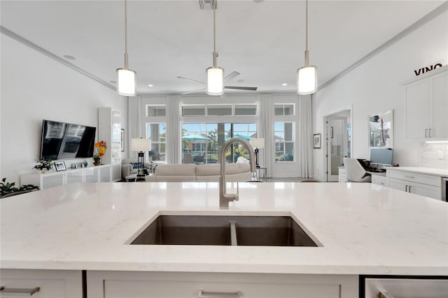 kitchen featuring light stone countertops, decorative light fixtures, an island with sink, sink, and ceiling fan