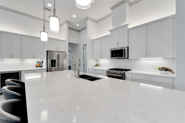 kitchen featuring appliances with stainless steel finishes, beverage cooler, hanging light fixtures, light stone counters, and sink