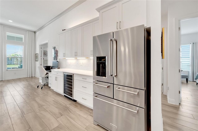 kitchen featuring high quality fridge, white cabinets, beverage cooler, backsplash, and crown molding