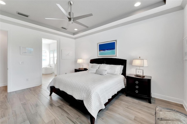 bedroom with ceiling fan, a tray ceiling, and connected bathroom