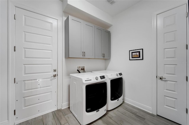 clothes washing area featuring cabinets, washer and clothes dryer, and light hardwood / wood-style flooring