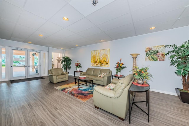 living room featuring hardwood / wood-style floors, a drop ceiling, and french doors