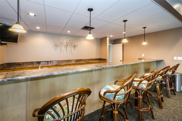 bar with stone counters, carpet floors, decorative light fixtures, and a drop ceiling