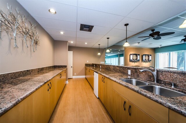 kitchen featuring pendant lighting, sink, dark stone counters, and light hardwood / wood-style flooring