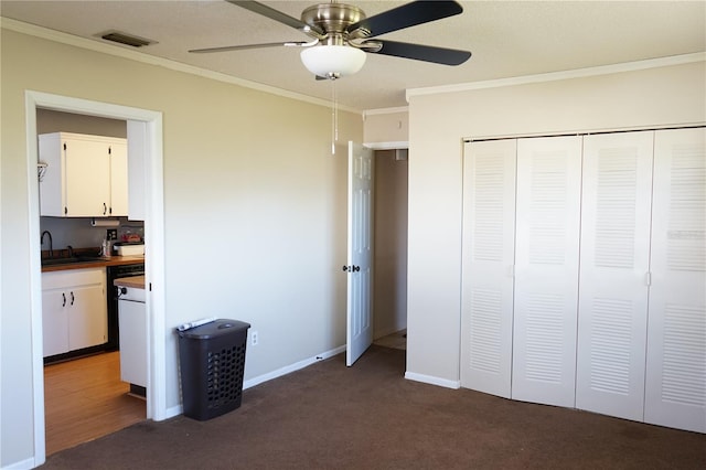 unfurnished bedroom featuring ceiling fan, sink, dark colored carpet, crown molding, and a closet