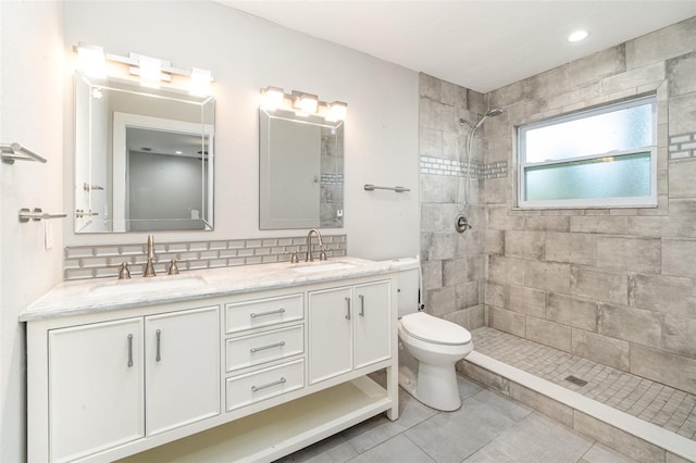 bathroom with a tile shower, tile patterned flooring, vanity, and toilet