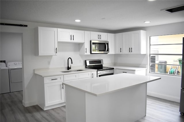 kitchen featuring stainless steel appliances, sink, white cabinets, independent washer and dryer, and a center island