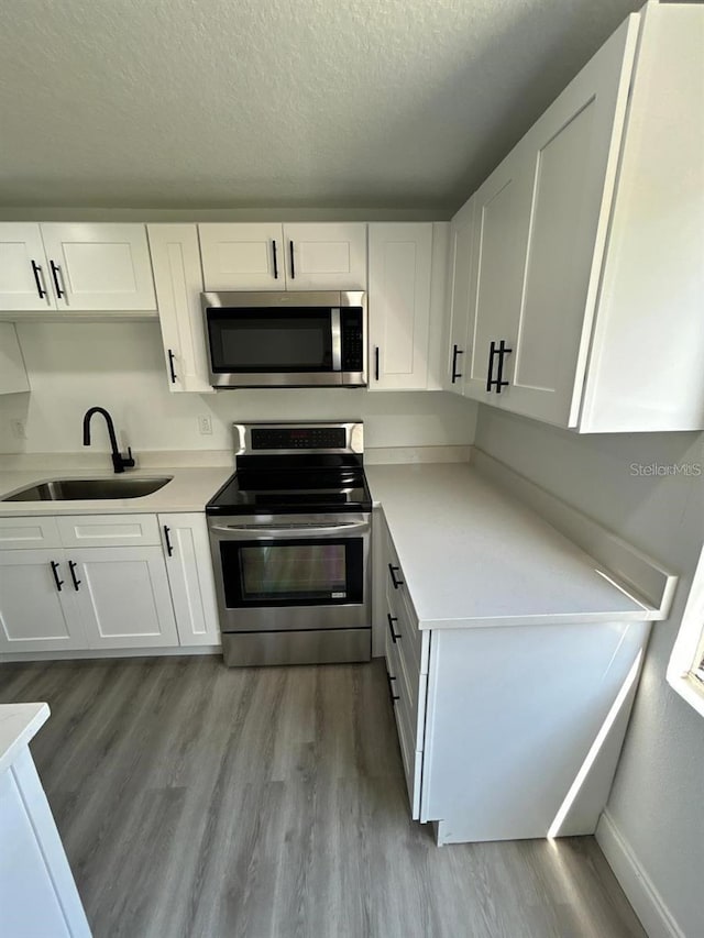 kitchen with white cabinets, sink, light wood-type flooring, a textured ceiling, and appliances with stainless steel finishes